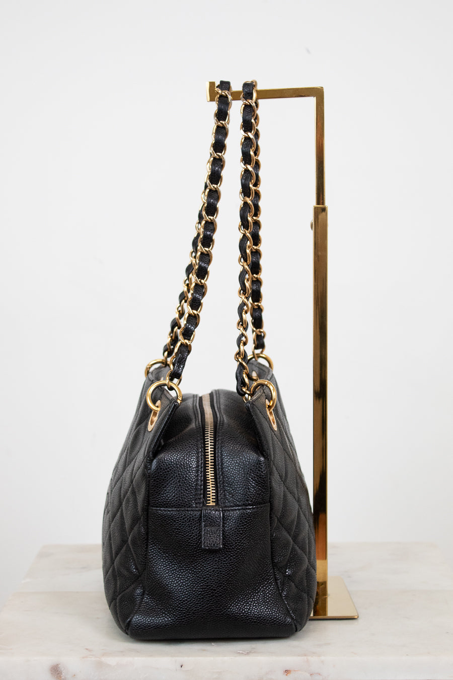 Black quilted handbag with gold chain strap on a white background