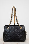 Black quilted handbag with gold chain handle on a white background