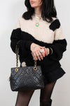 Person wearing a black and white sweater holding a Chanel handbag against a plain background