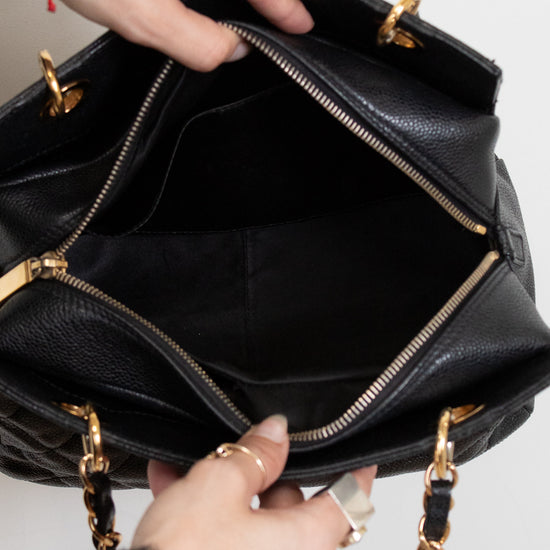 Black interior of handbag with gold accents held by a person's hands on a light gray background