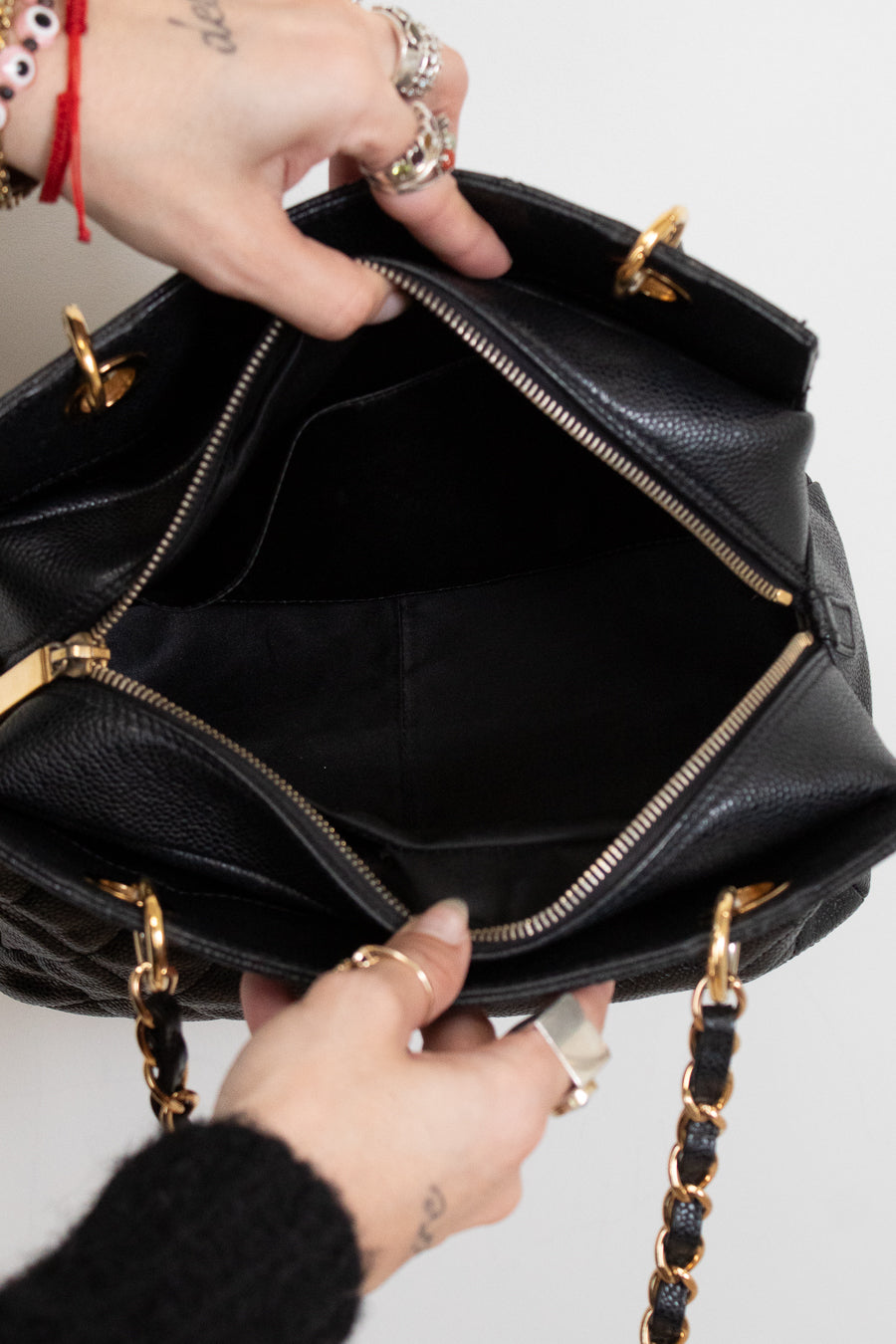 Black interior of handbag with gold accents held by a person's hands on a light gray background