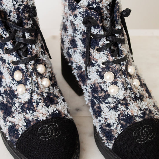A pair of black and white tweed lace up ankle boots with black leather toe caps featuring embroidered interlocking CC logo, silver-tone eyelets , black laces, and thick black rubber soles.