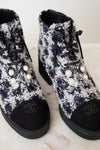 A pair of black and white tweed lace up ankle boots with black leather toe caps featuring embroidered interlocking CC logo, silver-tone eyelets , black laces, and thick black rubber soles.