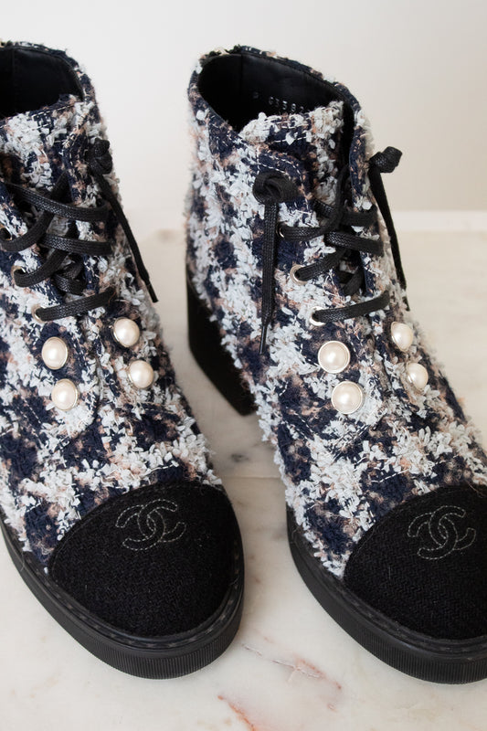 A pair of black and white tweed lace up ankle boots with black leather toe caps featuring embroidered interlocking CC logo, silver-tone eyelets , black laces, and thick black rubber soles.