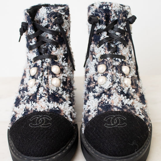 A pair of Chanel high-top ankle boots featuring a black, white, and pink floral tweed upper, black laces, decorative pearl embellishments, and a black suede toe cap with an embroidered Chanel logo.