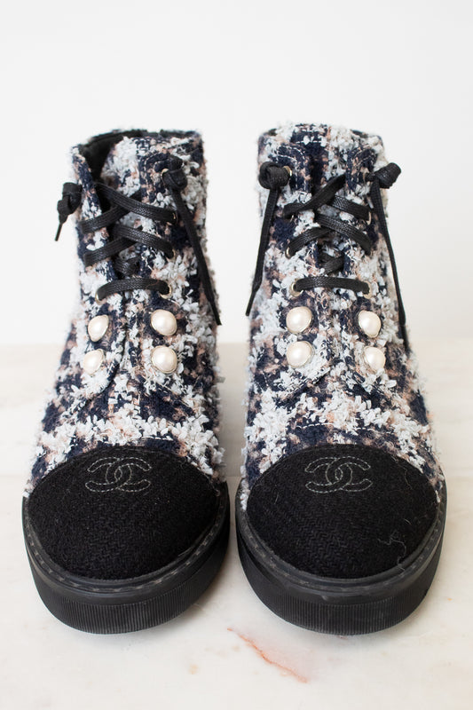 A pair of Chanel high-top ankle boots featuring a black, white, and pink floral tweed upper, black laces, decorative pearl embellishments, and a black suede toe cap with an embroidered Chanel logo.