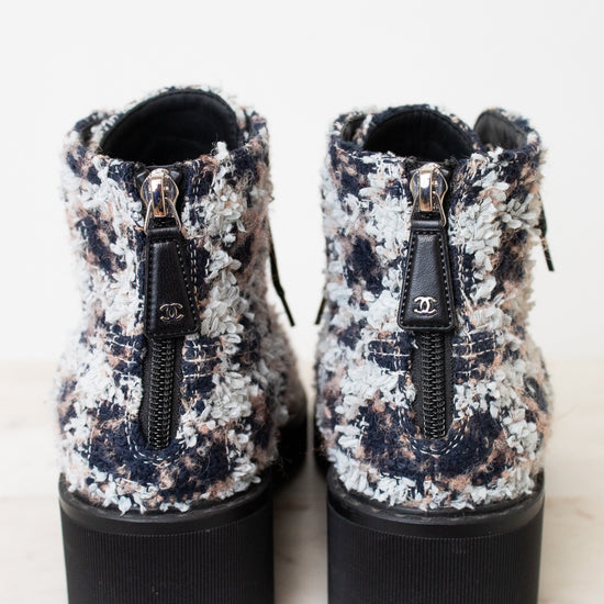 A pair of Chanel ankle boots with a black, white, and gray tweed pattern, featuring black platform soles and side zippers with the iconic interlocking CC logo.