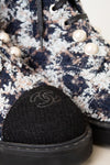 Close-up of a Chanel ankle boot featuring a navy, beige, and white tweed pattern, black laces, decorative pearl embellishments, and a black fabric cap with the iconic interlocking CC logo.