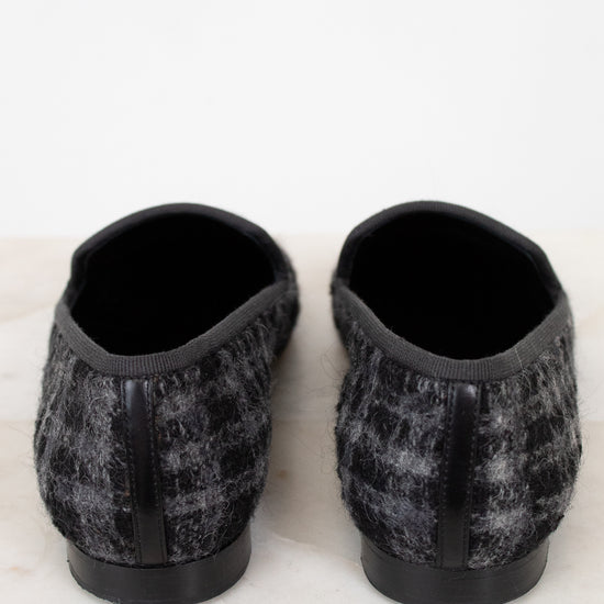 Pair of black and gray checkered tweed slippers on a white marble surface