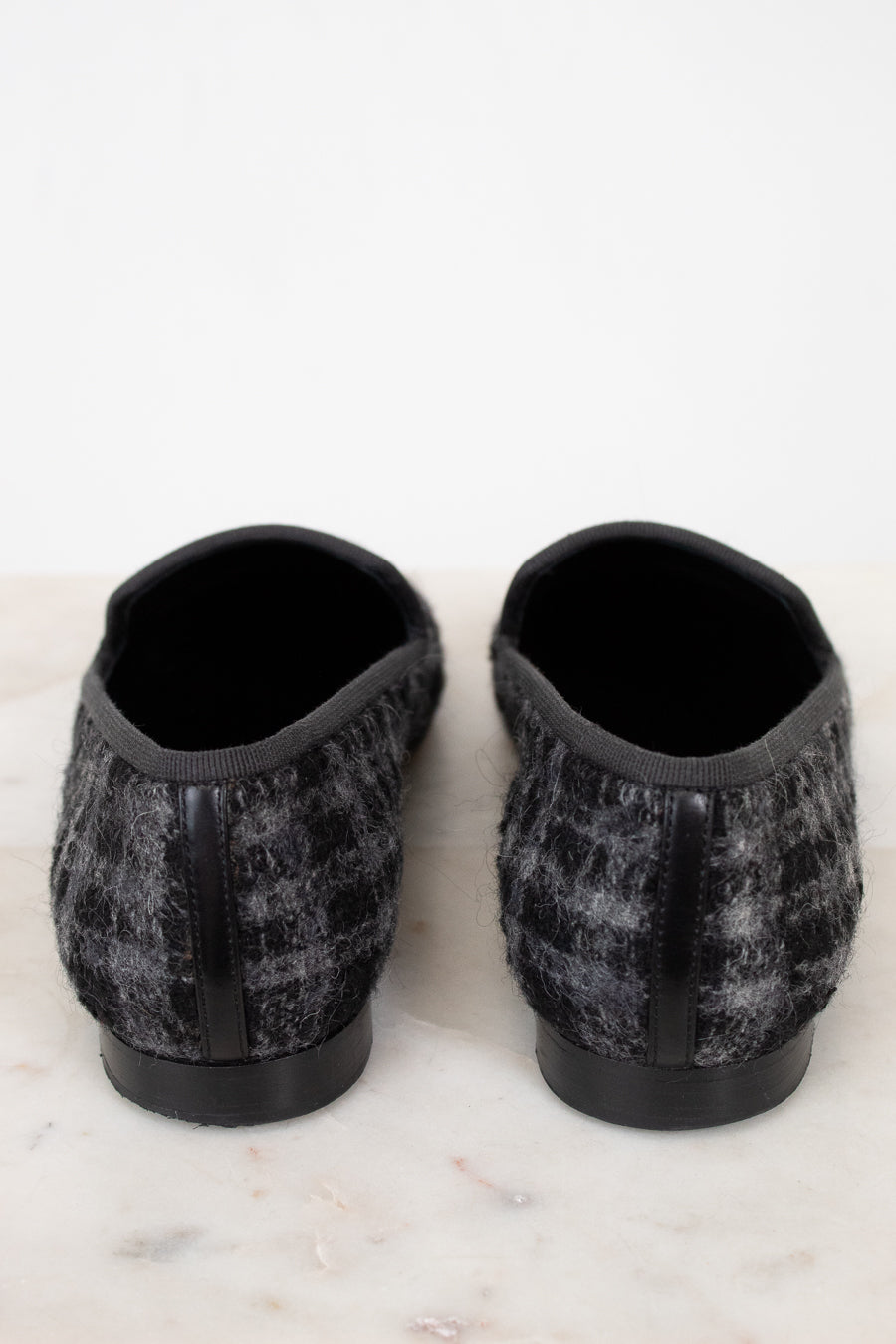 Pair of black and gray checkered tweed slippers on a white marble surface