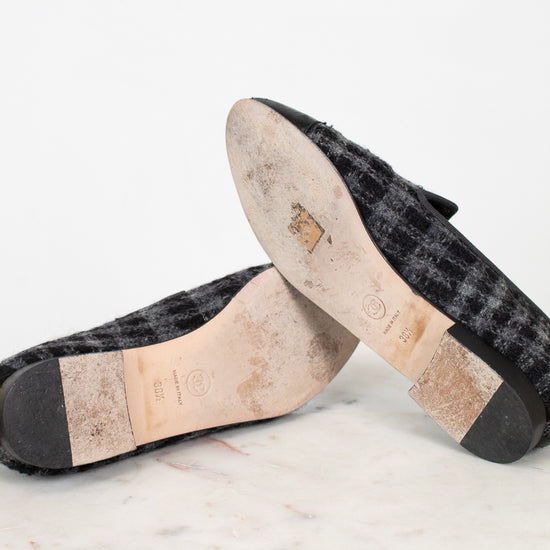 Bottom of pair of black tweed loafers on a light gray background