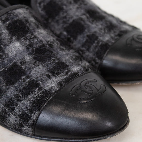 Pair of black and gray checkered tweed loafers with a brand logo on a marble surface