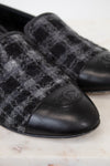 Pair of black and gray checkered tweed loafers with a brand logo on a marble surface