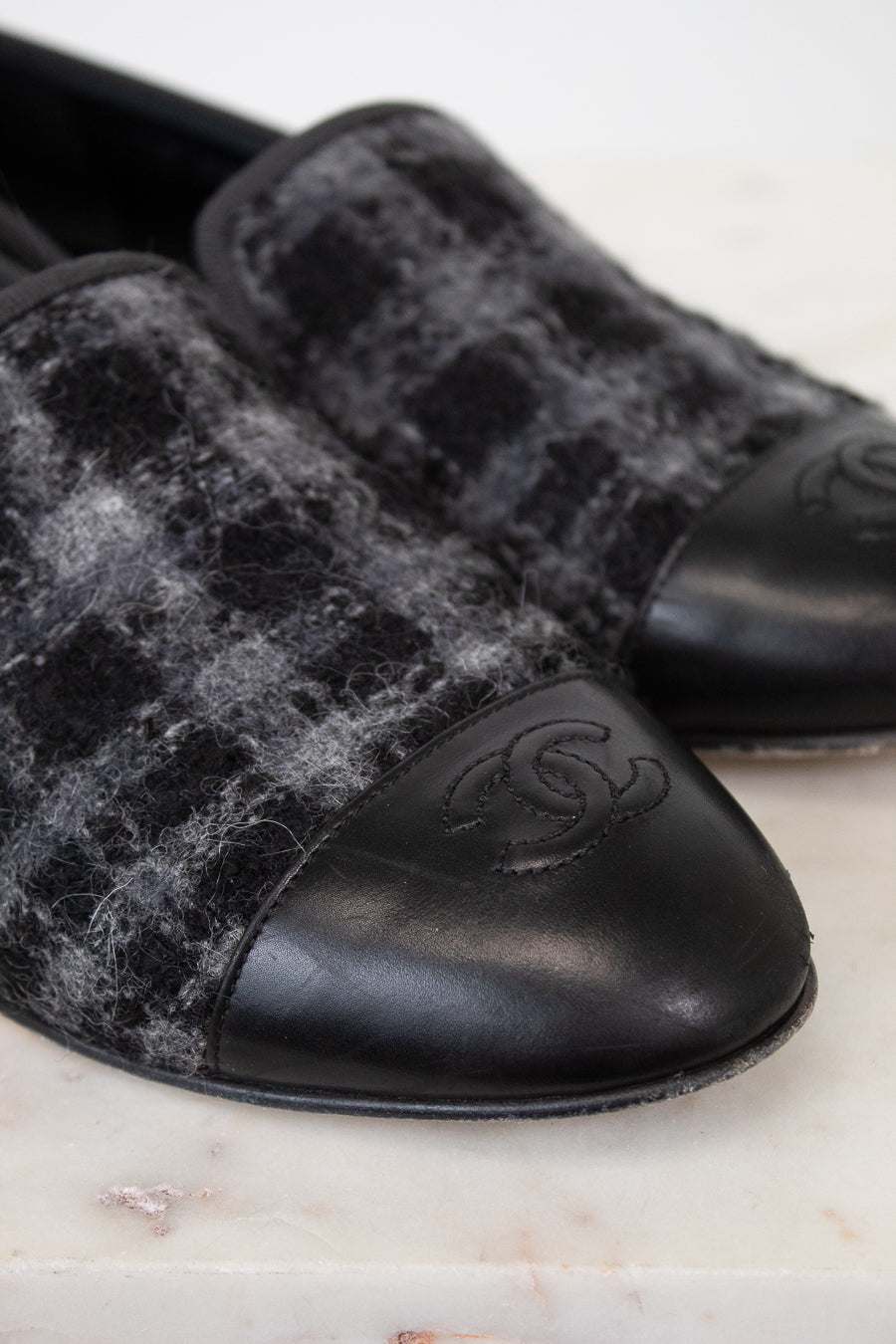 Pair of black and gray checkered tweed loafers with a brand logo on a marble surface