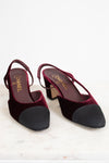 A pair of Chanel slingback block-heel pumps in deep burgundy velvet with black suede toe caps, displayed on a light marble surface against a white background.