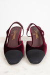 A pair of Chanel slingback pumps in deep burgundy velvet with black suede toe caps, shown from a top-down view on a light marble surface.