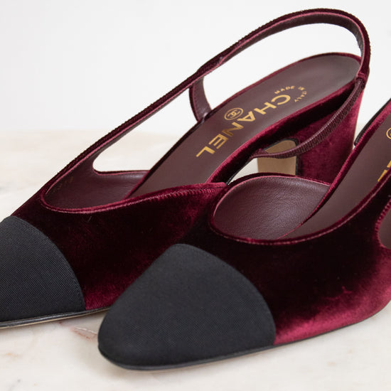 A pair of Chanel slingback pumps in deep burgundy velvet with black suede toe caps, displayed on a light marble surface.