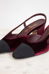 A pair of Chanel slingback pumps in deep burgundy velvet with black suede toe caps, displayed on a light marble surface.