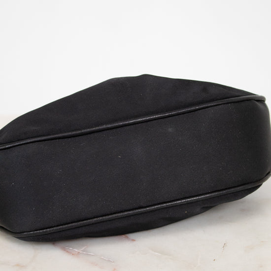 A black satin pouch bag with black leather piping, resting on a white marble surface against a white background.