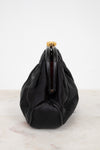 A black leather and satin shoulder bag with a gathered, slouchy silhouette and a gold-tone metal clasp closure, shown from the side on a light marble surface against a white background.