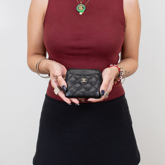 Person wearing a burgundy top and black skirt holding a black Chanel wallet against a plain background