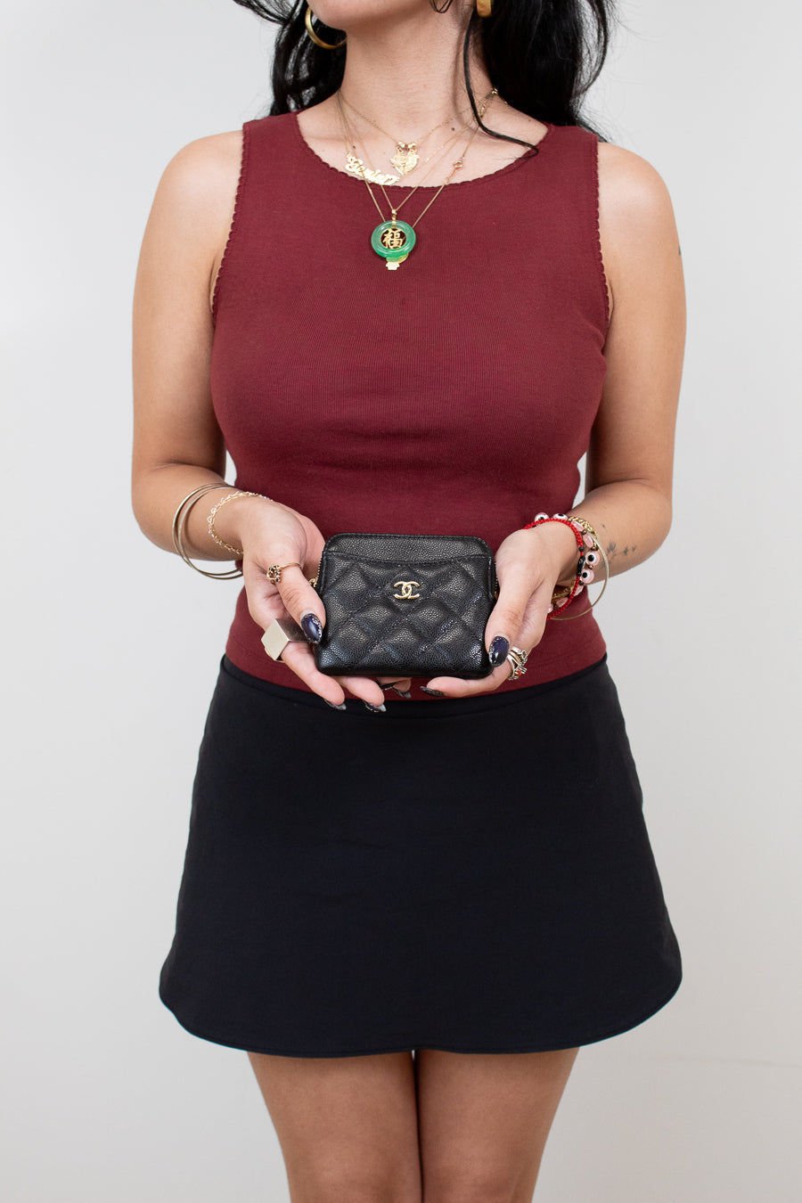 Person wearing a burgundy top and black skirt holding a black Chanel wallet against a plain background