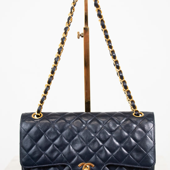 Navy blue quilted handbag with gold chain strap on a white background
