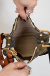 Close-up of a hand holding an open olive leather handbag with gold accents.
