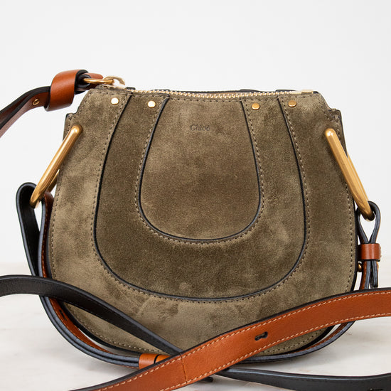 Olive suede handbag with a brown strap on a white background