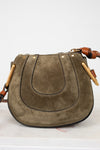 Olive suede handbag with leather strap and gold hardware on a white background