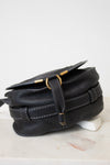 A black pebbled leather crossbody bag with gold-tone hardware, displayed on a white marble surface against a white background.