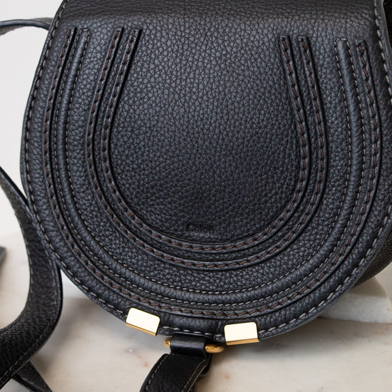 A black pebbled leather saddle bag with gold-tone hardware, resting on a light marble surface.