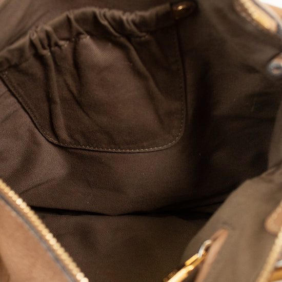 Close-up of the interior of a taupe-brown handbag, showing a dark brown fabric pocket with a gold-tone zipper pull and a gold zipper along the opening. A hand with red nail polish is holding the top edge.