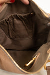Close-up of the interior of a taupe-brown handbag, showing a dark brown fabric pocket with a gold-tone zipper pull and a gold zipper along the opening. A hand with red nail polish is holding the top edge.
