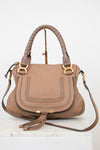 A structured taupe leather handbag with gold-tone hardware, dual top handles, and a detachable shoulder strap, displayed on a white marble block against a white background.