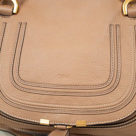 A close-up of a taupe brown pebbled leather handbag with gold-tone hardware and a matching leather strap resting in front.