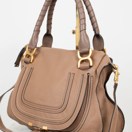 A structured taupe leather handbag with gold-tone hardware, featuring two braided top handles, a front flap pocket, and a detachable shoulder strap, photographed on a light neutral background.