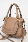 A structured taupe leather handbag with gold-tone hardware, featuring two braided top handles, a front flap pocket, and a detachable shoulder strap, photographed on a light neutral background.