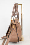 A taupe brown pebbled leather handbag with gold-tone hardware, displayed on a minimalist gold metal stand against a clean white background.