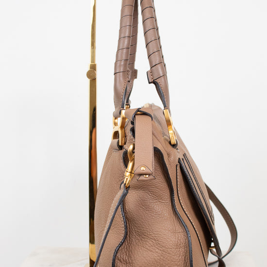 A brown leather handbag with gold-tone hardware, displayed on a gold metal stand against a white background.