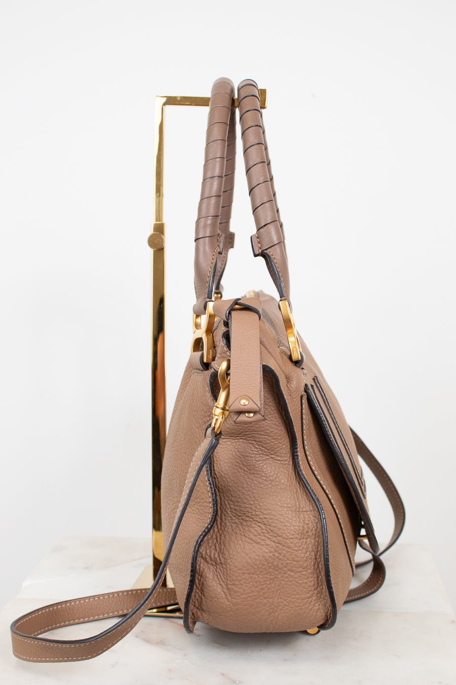 A brown leather handbag with gold-tone hardware, displayed on a gold metal stand against a white background.