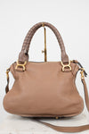 A taupe brown pebbled leather handbag with a braided top handle, gold-tone hardware, and a matching shoulder strap, displayed on a stand against a white background.