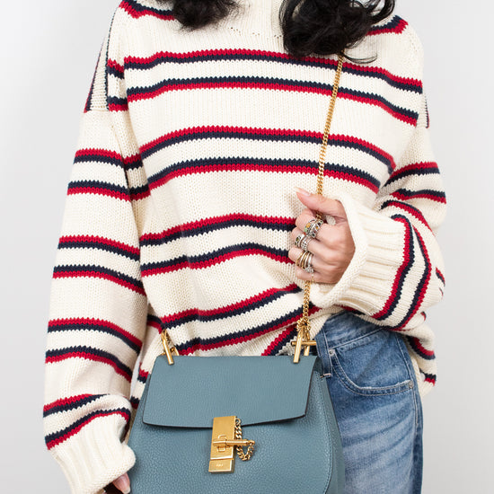 Person wearing a striped sweater and holding a blue handbag against a plain background