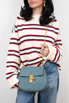 Person wearing a striped sweater and holding a blue handbag against a plain background