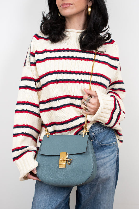 Person wearing a striped sweater and holding a blue handbag against a plain background