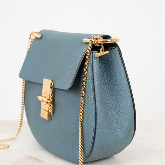 Blue handbag with gold chain and clasp on a white background