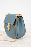 Blue handbag with gold chain and clasp on a white background