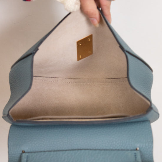 Close-up of a hand holding a blue and beige handbag with a gold clasp.