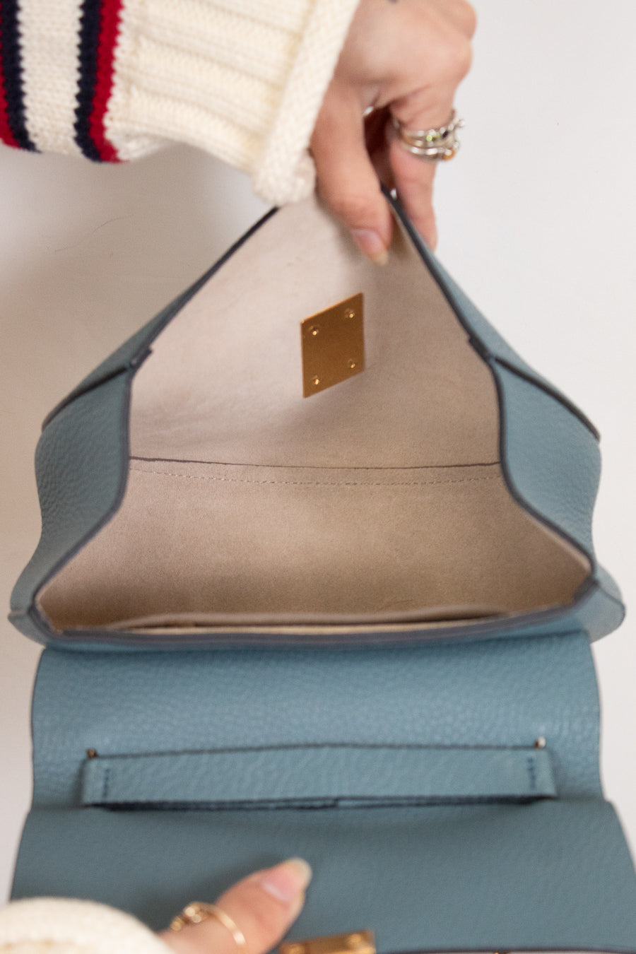 Close-up of a hand holding a blue and beige handbag with a gold clasp.