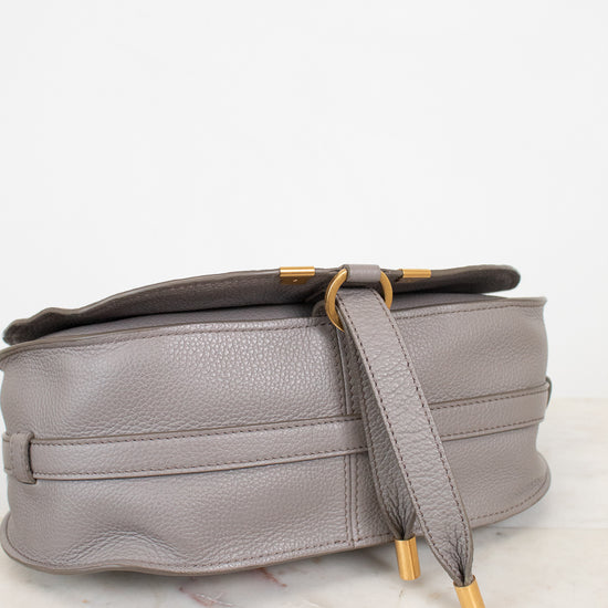 A light gray pebbled leather shoulder bag with gold-tone hardware, resting on a white marble surface against a white background.